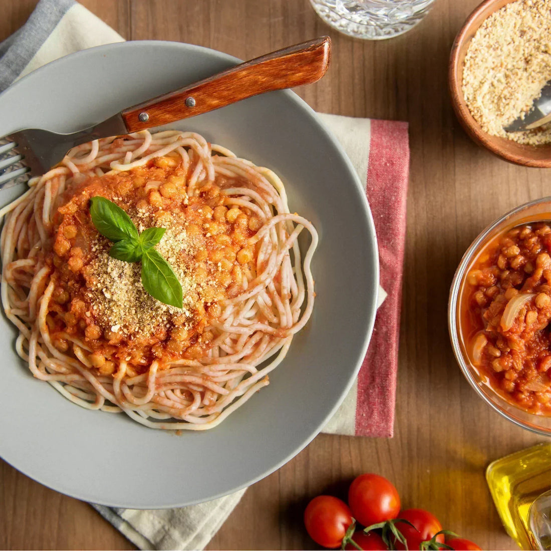 Teller mit KOMEKO Vollkornreis-Spaghetti, getoppt mit Linsen-Walnuss-Bolognese und frischen Kräutern garniert.