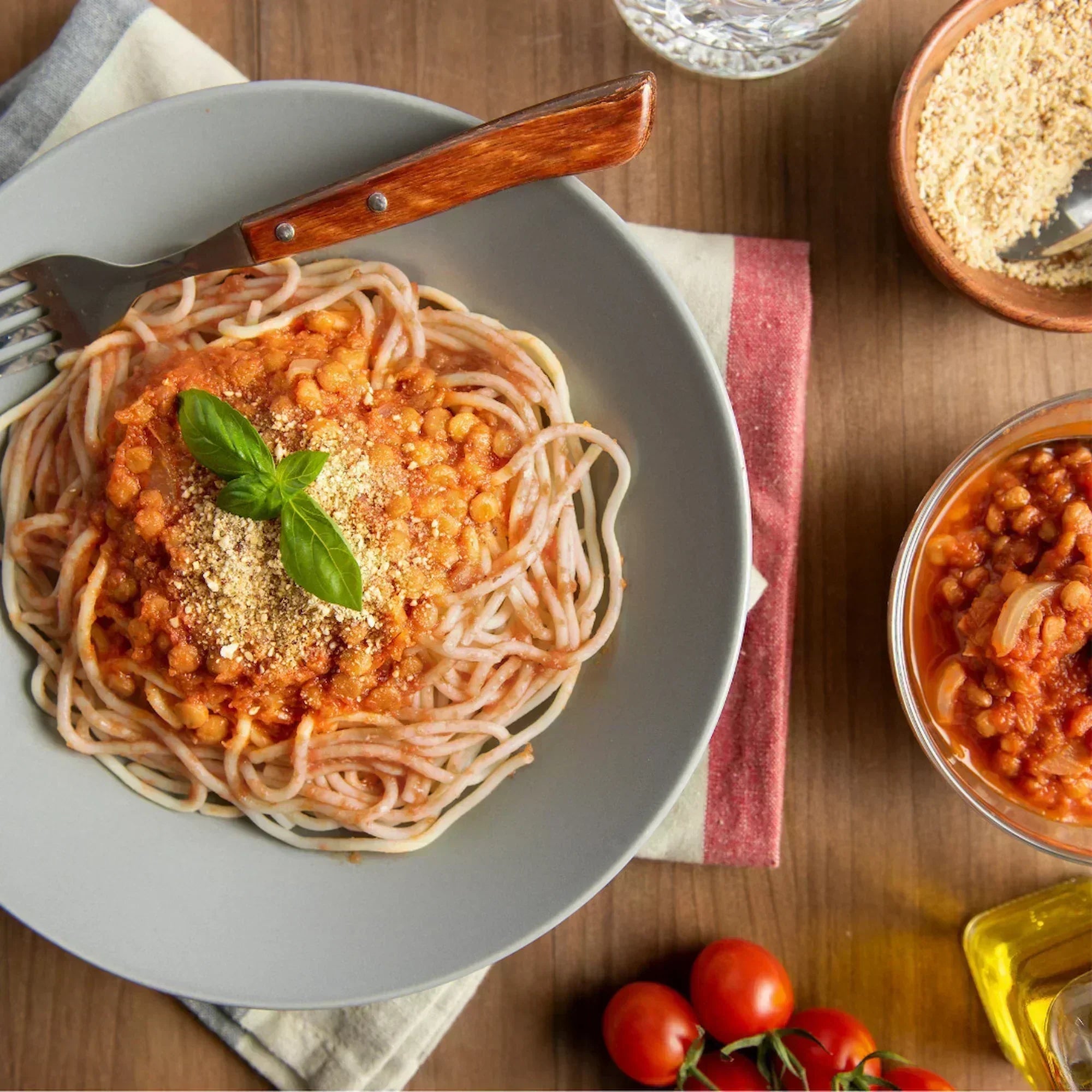 Teller mit KOMEKO Vollkornreis-Spaghetti, getoppt mit Linsen-Walnuss-Bolognese und frischen Kräutern garniert.
