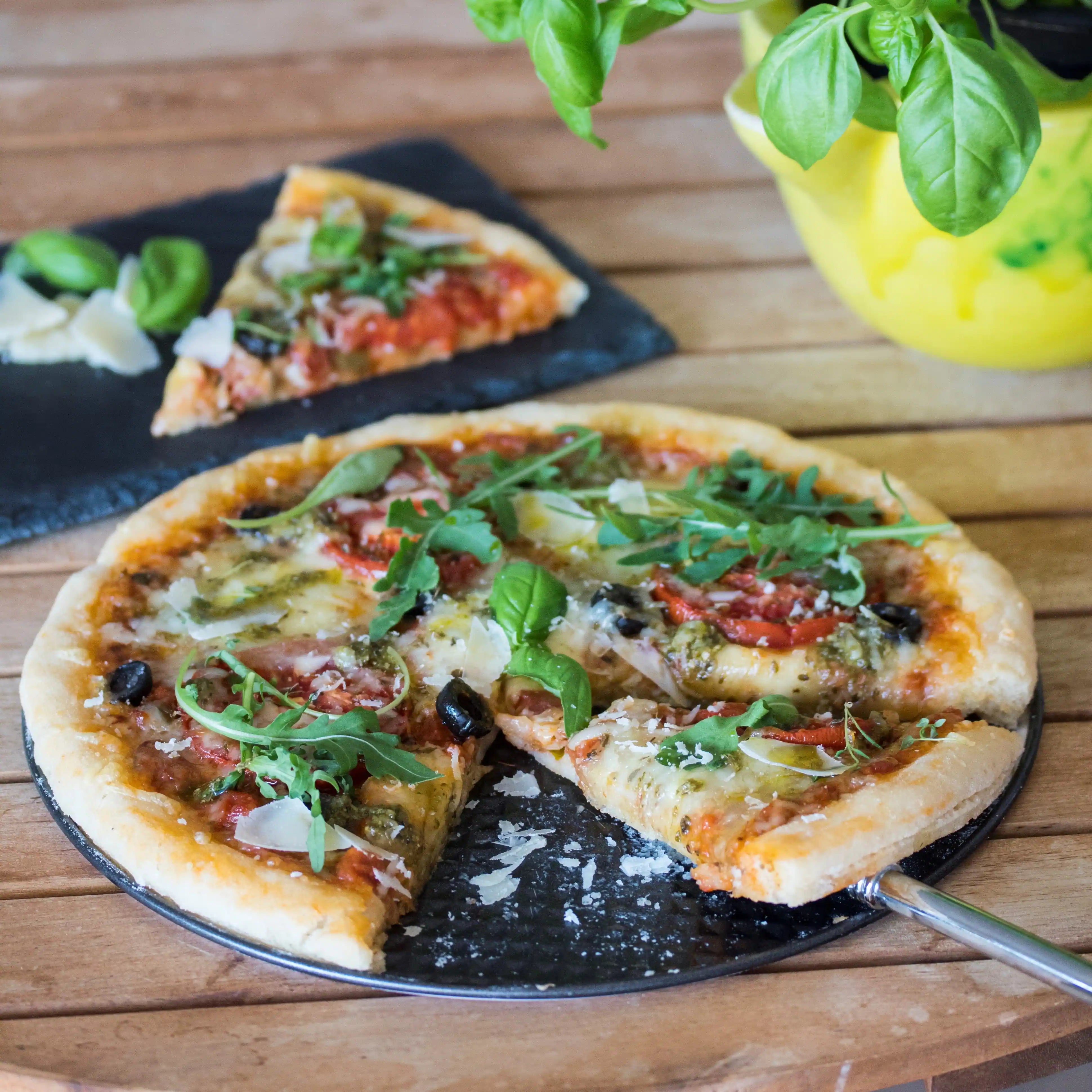 Glutenfreie Pizza mit fluffigem Boden, belegt mit Paprika, Oliven und frischem Rucola.