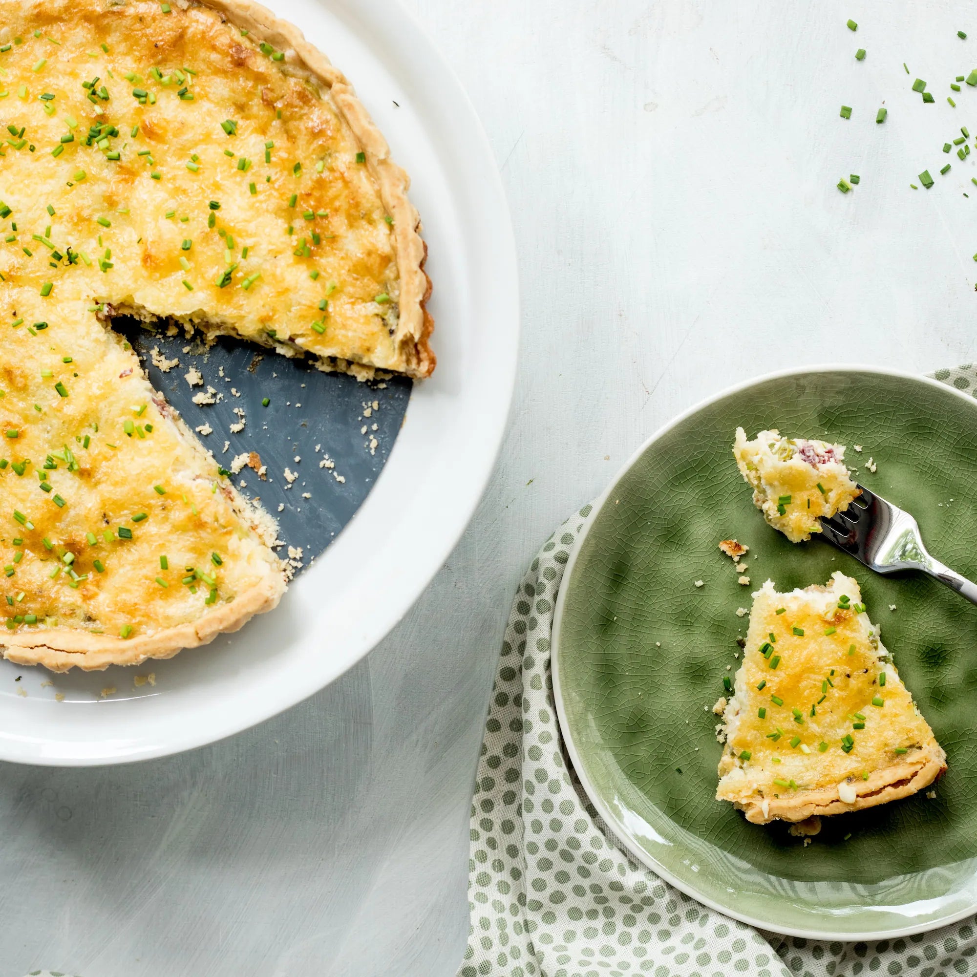 Goldbraun gebackene glutenfreie Quiche mit Porree, Schinken und geschmolzenem Käse, in Stücke geschnitten und mit frischem Schnittlauch garniert.